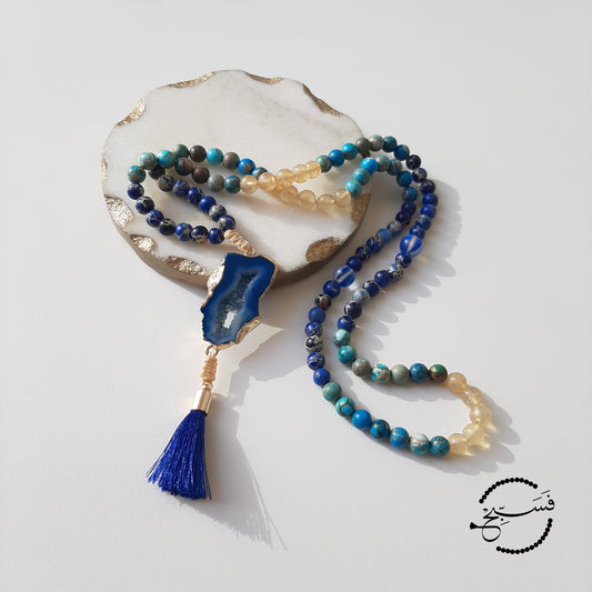 Sea sediment in shades of blue, with smoky quartz beads. The pendant is agate, in a striking blue colour.  Packaged in a luxurious pouch and a gift box.  99 beads